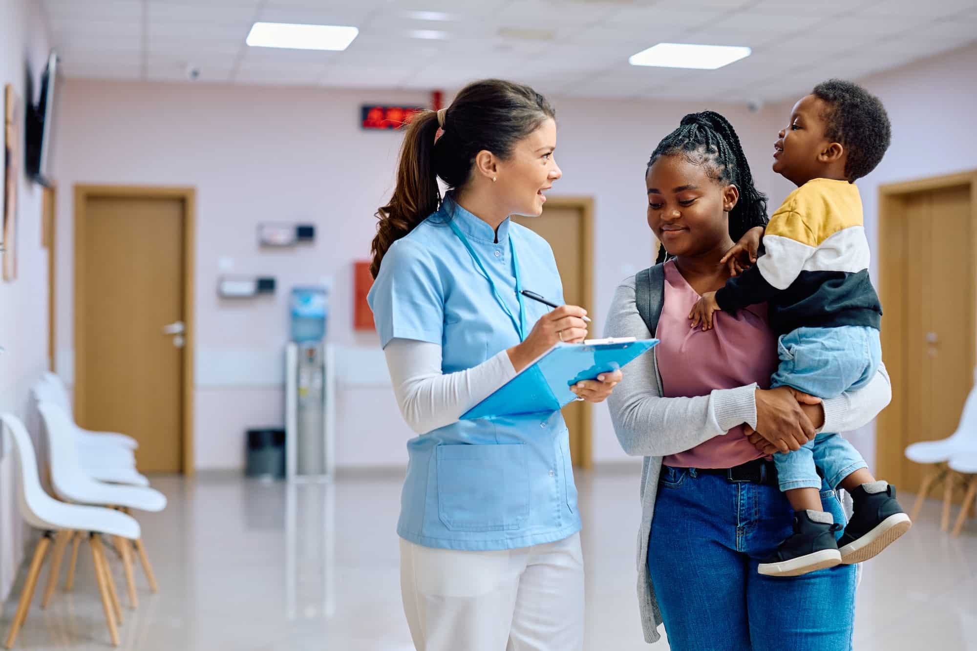 Happy nurse communicating with black mother and son in waiting room at pediatric clinic.